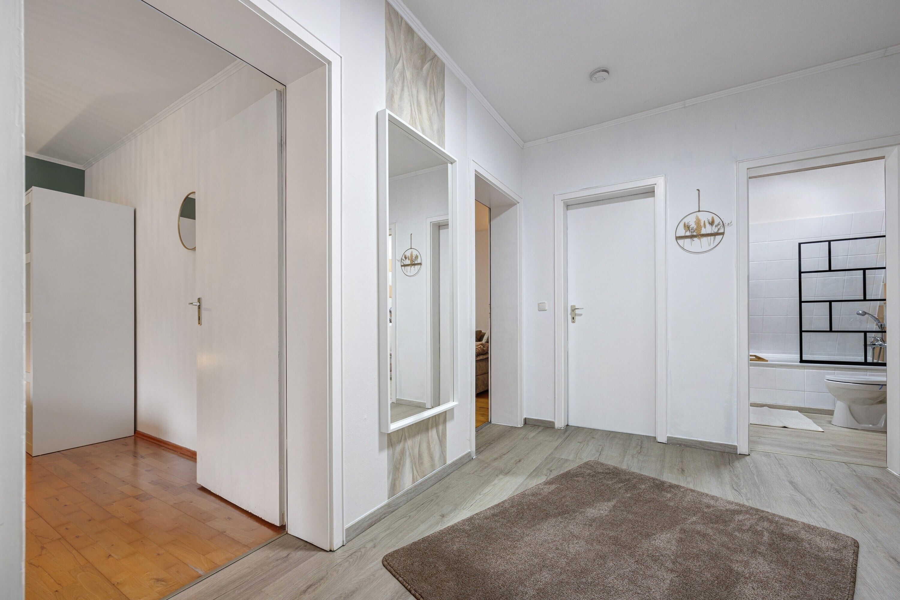 A hallway with white doors, a mirror, and a brown rug.