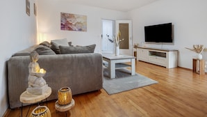 A modern living room with a sofa, a TV, a small table, and decorative items. - Apartment 'Ferienwohnung Berti' with Balcony and Infrared Sauna (Heeßen)