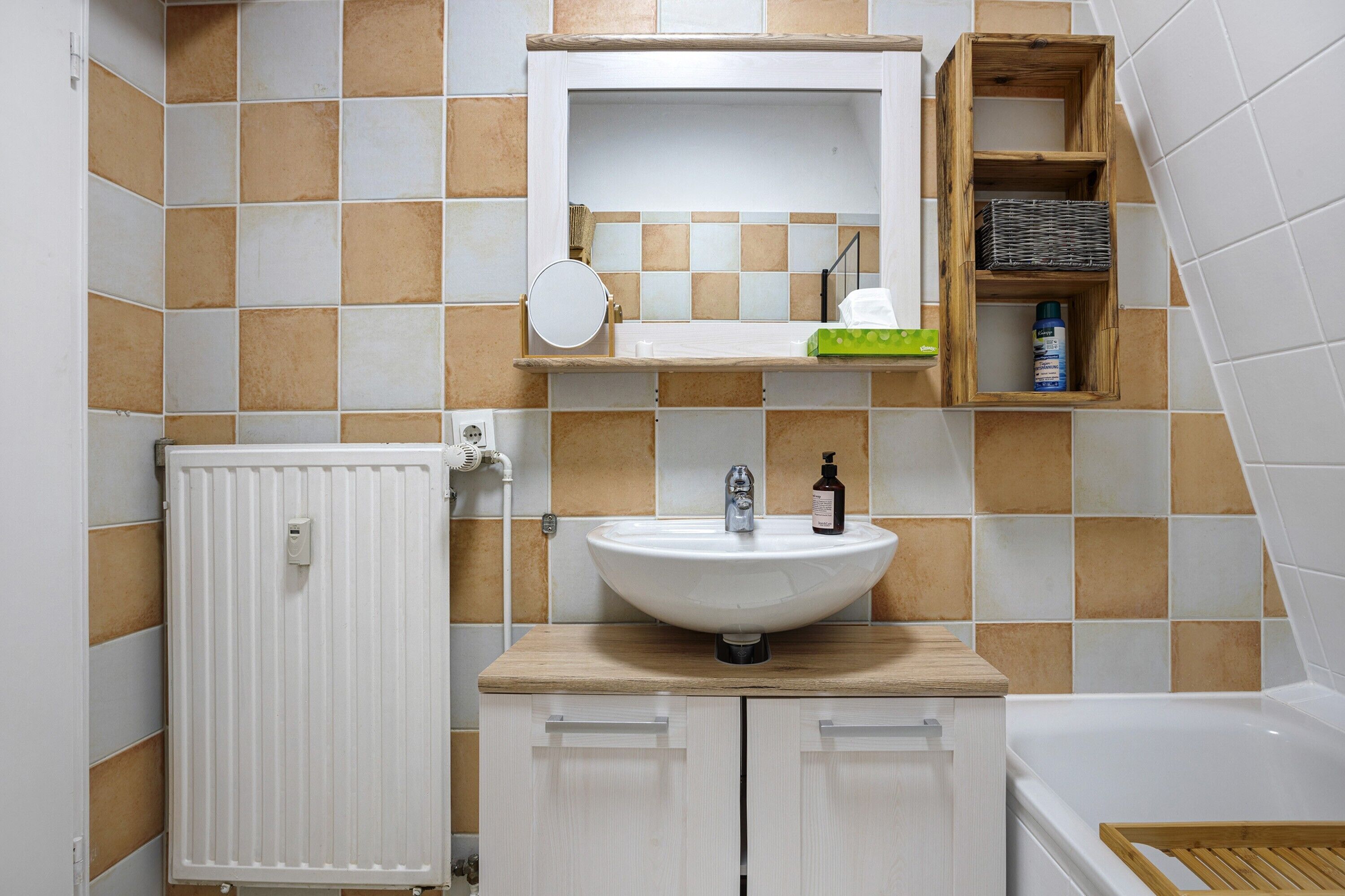 A bathroom with a white sink, mirror, and wooden shelf with toiletries.