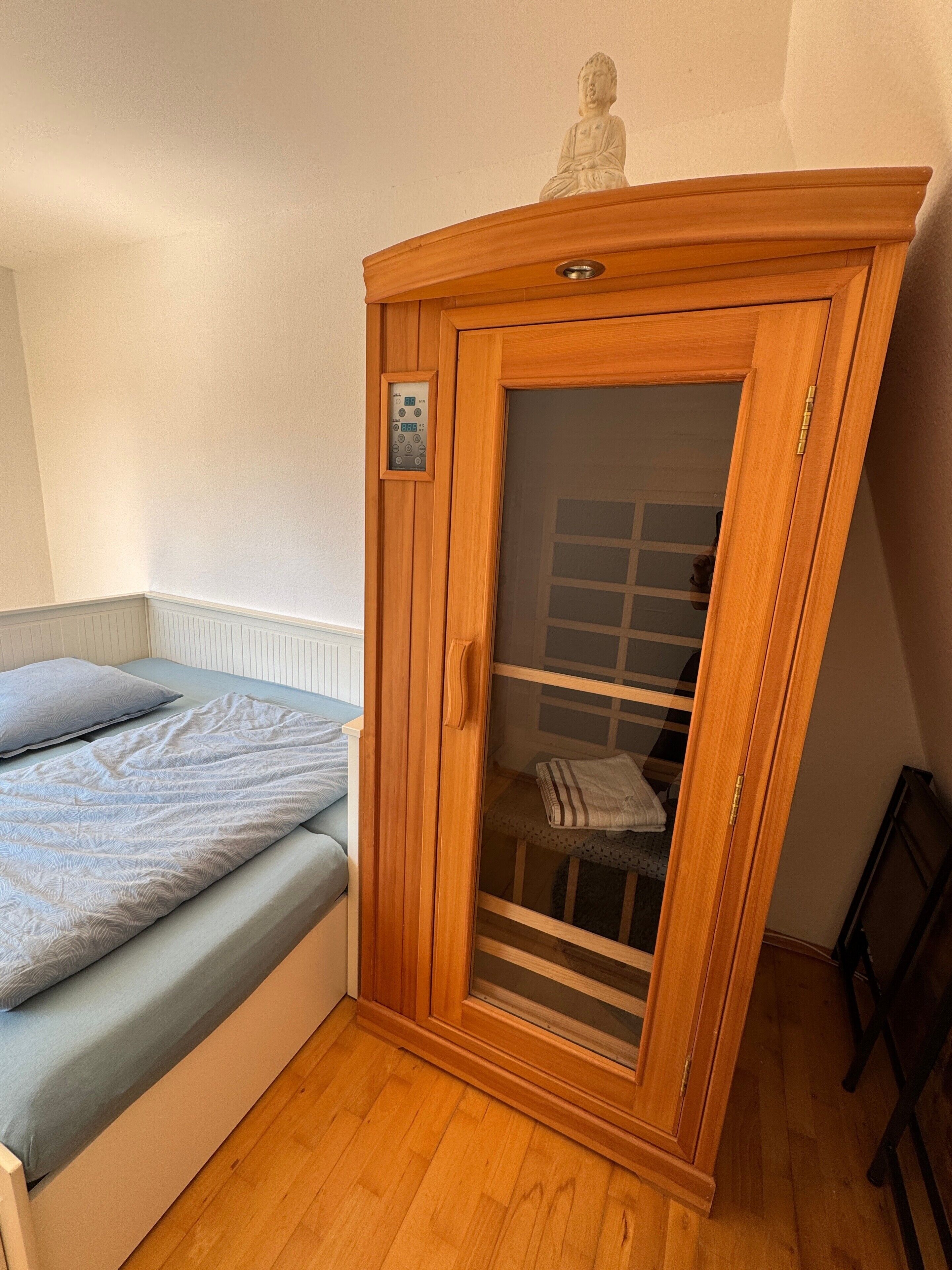 Un dormitorio con una cama, un armario de madera, una pequeña estatua y una ventana.