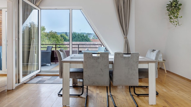 A dining area with a table and chairs, a sliding glass door leading to an outdoor balcony, and a hanging plant. - Apartment 'Ferienwohnung Berti' with Balcony and Infrared Sauna (Heeßen)