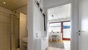 A bathroom with a shower, toilet, and sink. There is a door leading to a dining area with a table and chairs. - Apartment 'Edda 3' with Shared Garden, Balcony and Wi-Fi (Meldorf)