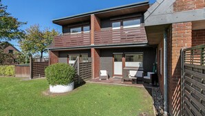 A two-story residential building with a brick facade, a small front yard with a hedge, and a visible garage door. - Apartment 'Edda 3' with Shared Garden, Balcony and Wi-Fi (Meldorf)