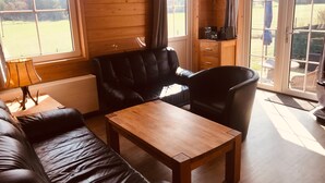 A wooden interior with a sofa, a table, a clock, and a view through a window. - Holiday Home 'Wolfshütte' with Private Terrace, Garden and Wi-Fi (Hillesheim)