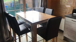 A wooden interior with a dining table and chairs, a view of a garden through large windows, and a kitchen area. - Holiday Home 'Wolfshütte' with Private Terrace, Garden and Wi-Fi (Hillesheim)