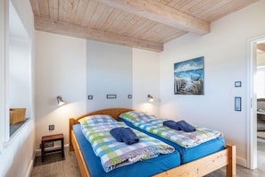 Une chambre avec deux lits, une tête de lit en bois, des lampes fixées au mur et un tableau.