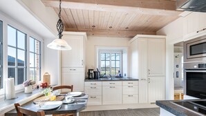 A modern kitchen with white cabinets, a wooden ceiling, and a dining area with a table set for two. - Holiday Home 'Lüthjes Friesenhaus' with Private Terrace, Garden and Wi-Fi (Rodenäs)