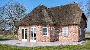 A brick building with a thatched roof, large windows, and a paved entrance. - Holiday Home 'Lüthjes Friesenhaus' with Private Terrace, Garden and Wi-Fi (Rodenäs)