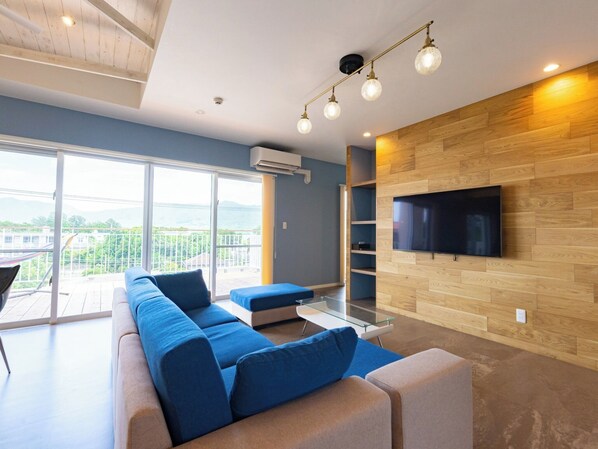Relax in this stylish living room with a large sectional sofa, flat-screen TV, and sliding glass door to a balcony with a scenic view.