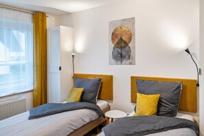 Une chambre d’hôtel avec deux lits, une petite table ronde, une œuvre d’art accrochée au mur et une fenêtre avec des rideaux.
