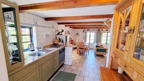 Eine Küche mit Holzbalken, einem Spülbecken, einem Geschirrspüler, einer Essecke mit Stühlen und einem Schrank mit Glastüren.