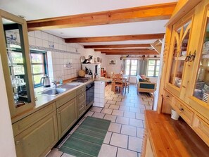A kitchen with wooden beams, a sink, a dishwasher, a dining area with chairs, and a cabinet with glass doors.
