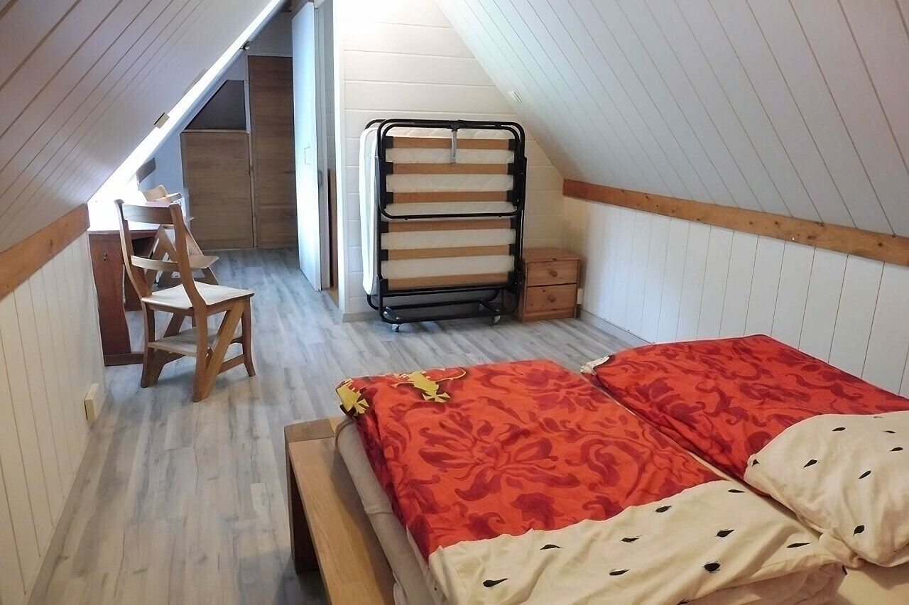 Une petite chambre mansardée, chaleureuse et accueillante, avec un lit, une chaise, un bureau en bois et un étendoir à linge en métal.