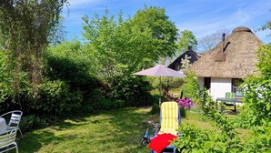 Ein Haus mit einem Strohdach, einem Garten, einem blauen Stuhl und einem roten Kissen.