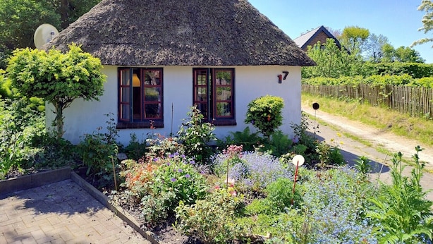 Ein weißes Haus mit Strohdach, Hausnummer 17, umgeben von einem Garten mit verschiedenen Pflanzen und Blumen.
