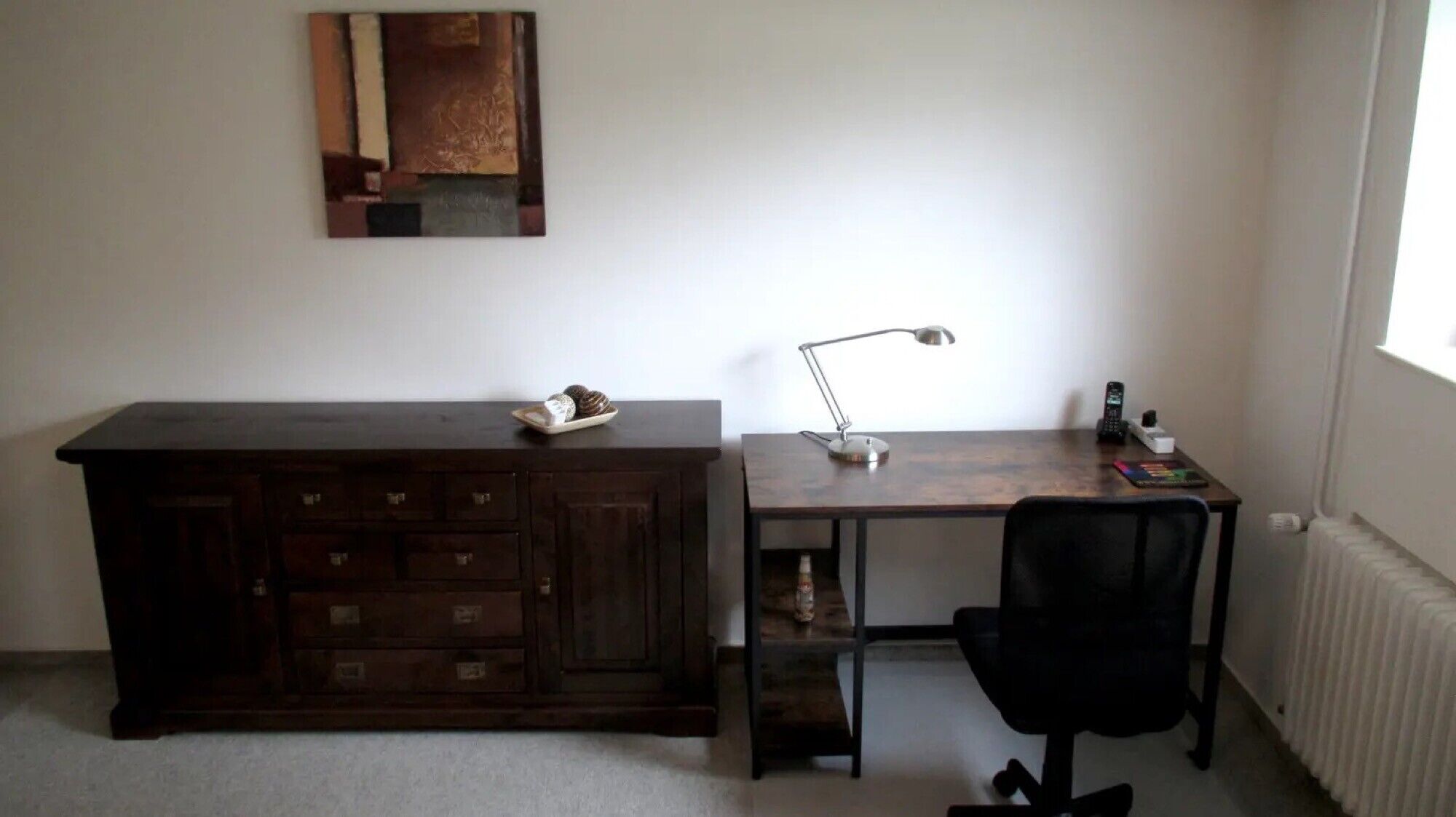 Un petit bureau comprenant un bureau en bois, une chaise, une lampe, un téléphone et un placard.