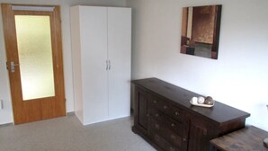 Una habitación con puerta de madera, un armario blanco, un aparador de madera oscura y una mesita pequeña.