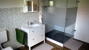 Un baño con tocador blanco, cabina de ducha con mampara de vidrio y baldosas estampadas.