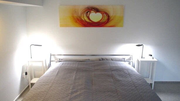 Un dormitorio con una cama, dos mesitas de noche, una lámpara de pared y un cuadro.