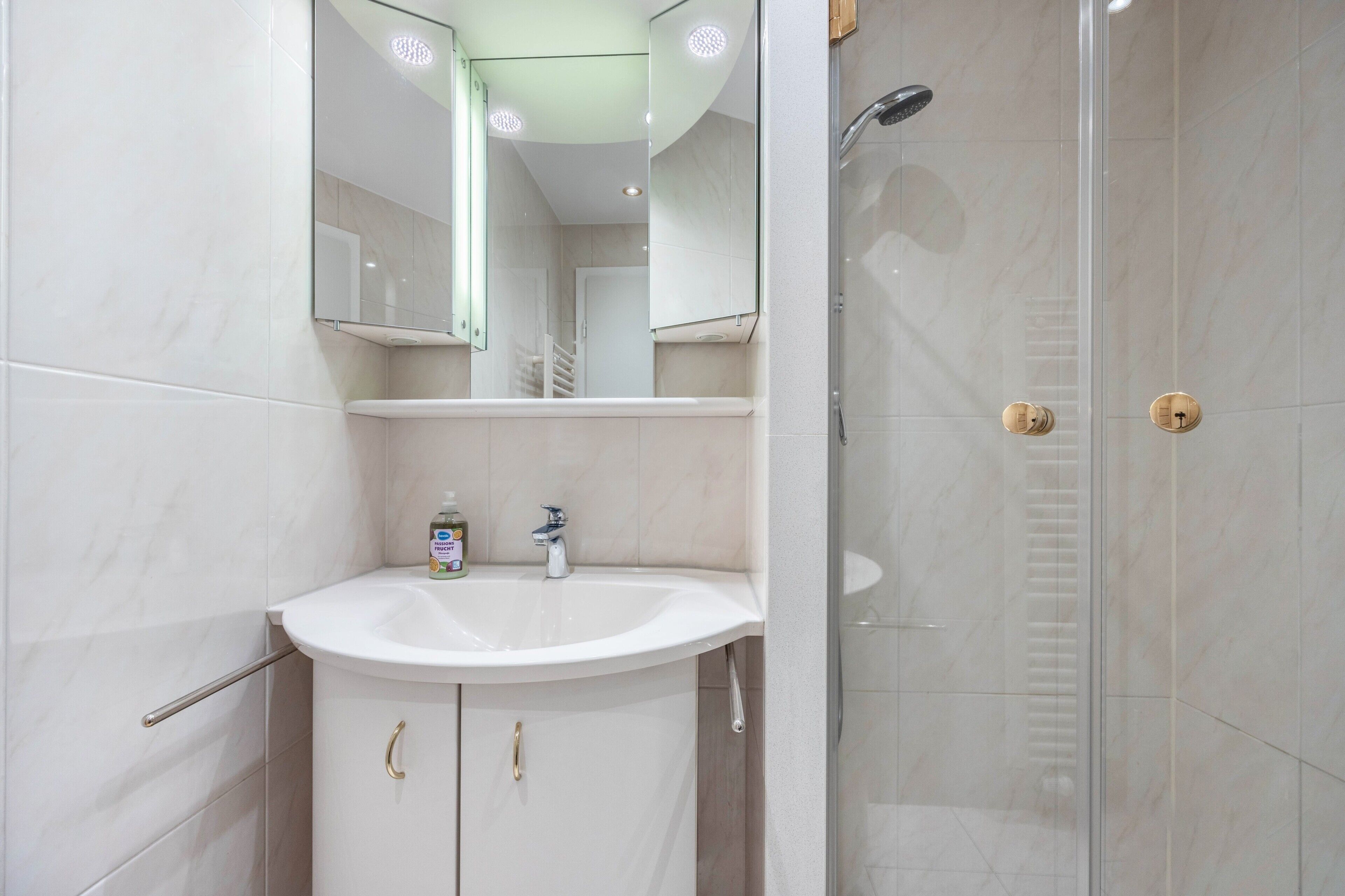 Un baño con lavamanos blanco, espejo y cabina de ducha de vidrio.
