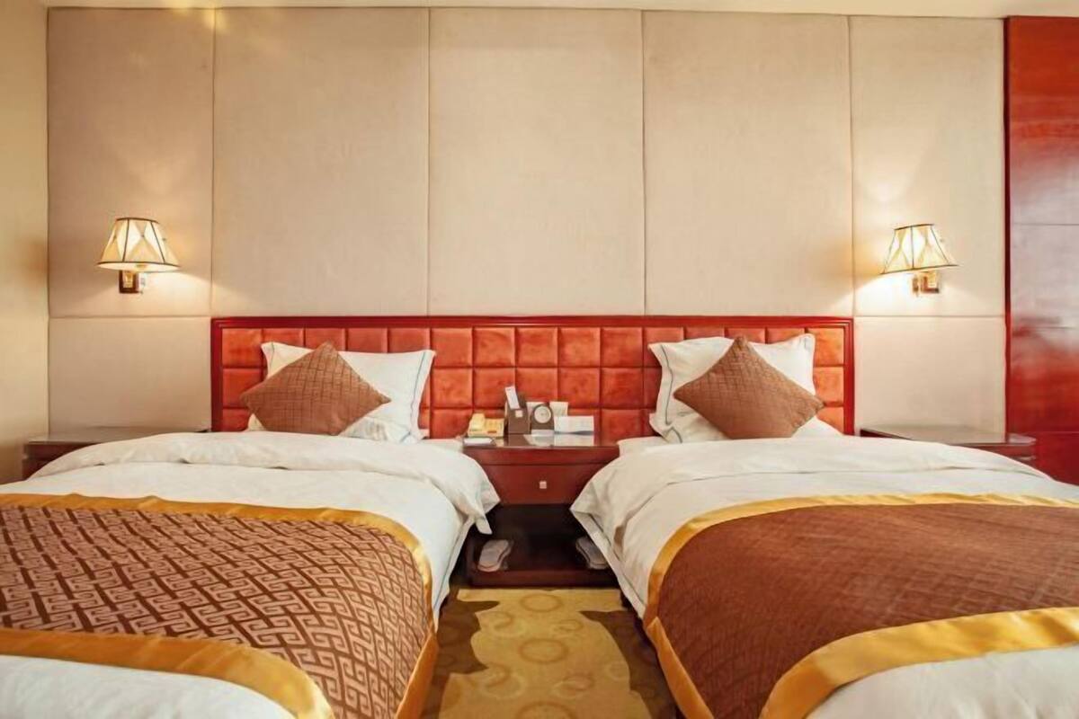A hotel room with two beds, a red headboard, bedside lamps, and a nightstand with a lamp.