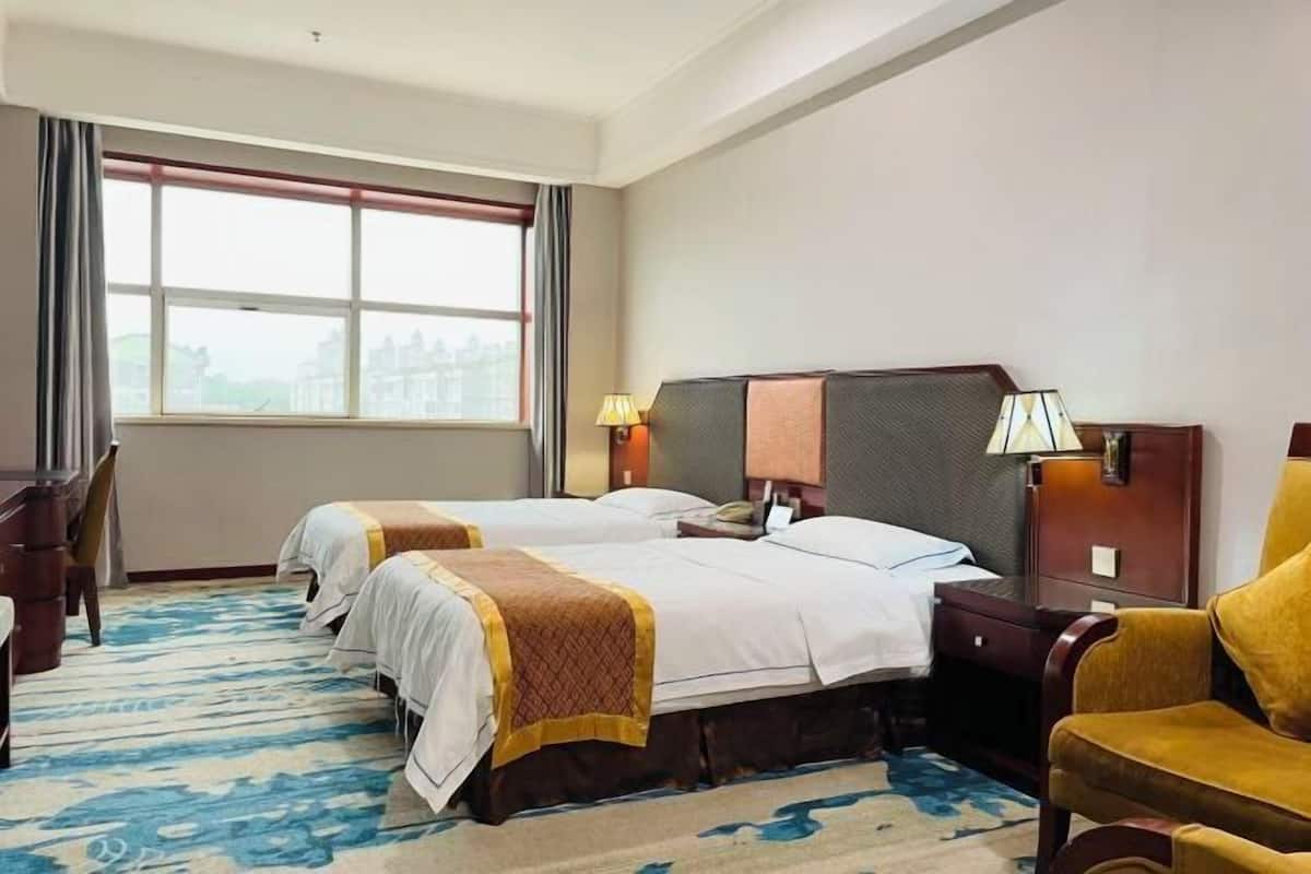 A hotel room with two beds, a desk, a chair, and a large window.