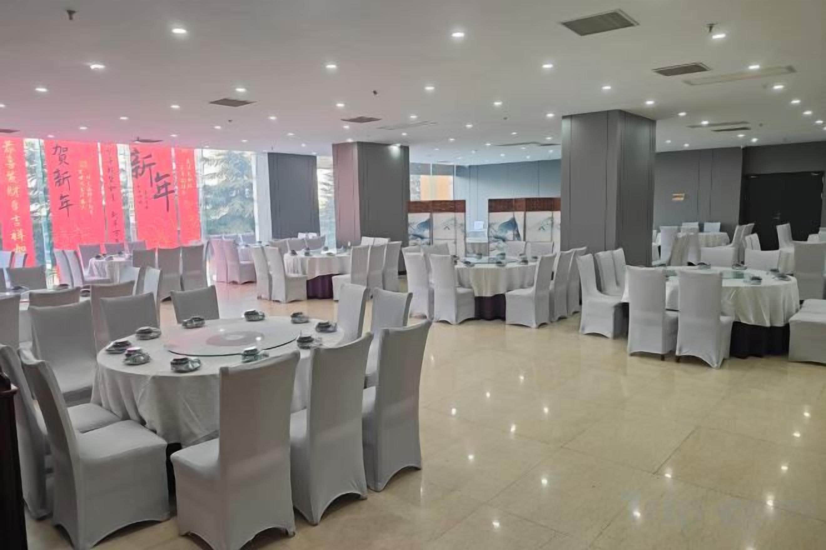 Un salón de banquetes con mesas y sillas redondas, ventanas amplias y una decoración de diseño moderno.