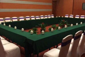 Une salle de conférence avec une longue table, des chaises et une nappe verte.