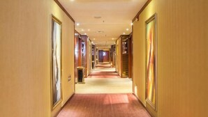 En hotellkorridor med ett mattbeklätt golv, trädörrar och inramade konstverk på väggarna.