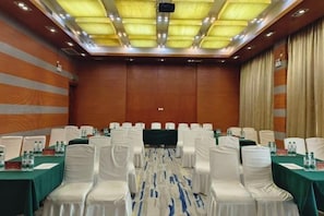Une salle de conférence avec des rangées de chaises blanches, des tables avec des bouteilles d’eau et une moquette verte.