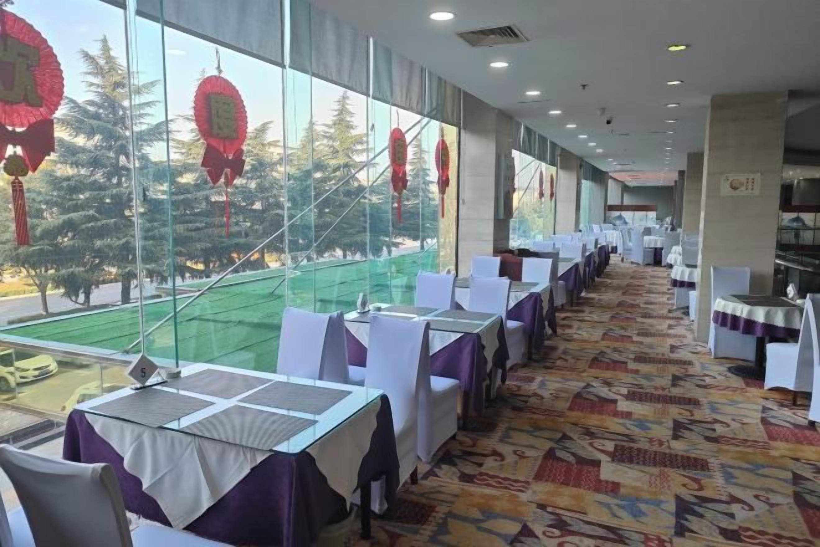 A restaurant with tables arranged in rows, large windows, and a view of trees outside.