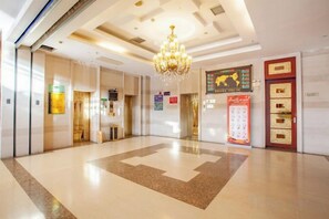 Un hall d’hôtel avec un lustre, un comptoir d’accueil et un mur orné d’une carte du monde et d’un calendrier.