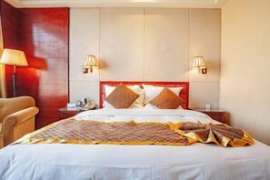 A hotel room with a bed, two bedside lamps, a nightstand, a chair, and a red accent wall. - Yongji Haina International Hotel (Yongji)