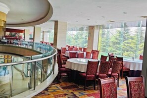 A restaurant with a central round table surrounded by chairs, a glass railing, and large windows offering a view of greenery. - Yongji Haina International Hotel (Yongji)