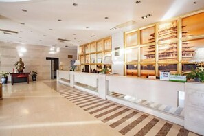 Un hall d’hôtel moderne avec un comptoir d’accueil, une statue et un sol à motifs.