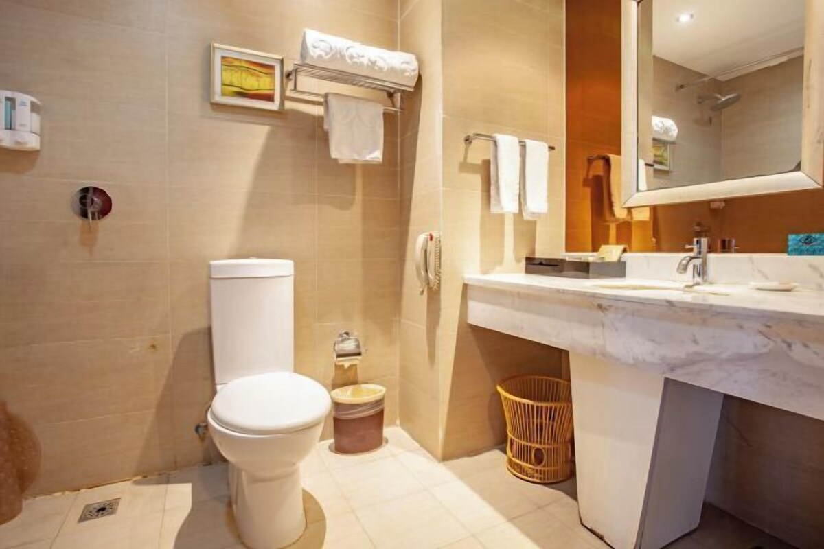 A bathroom with a toilet, sink, and mirror. There are towels and a basket.