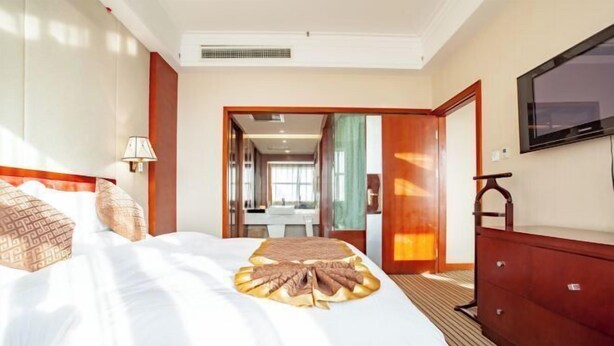 Habitación de hotel con una cama grande, un televisor montado en la pared y un aparador de madera.