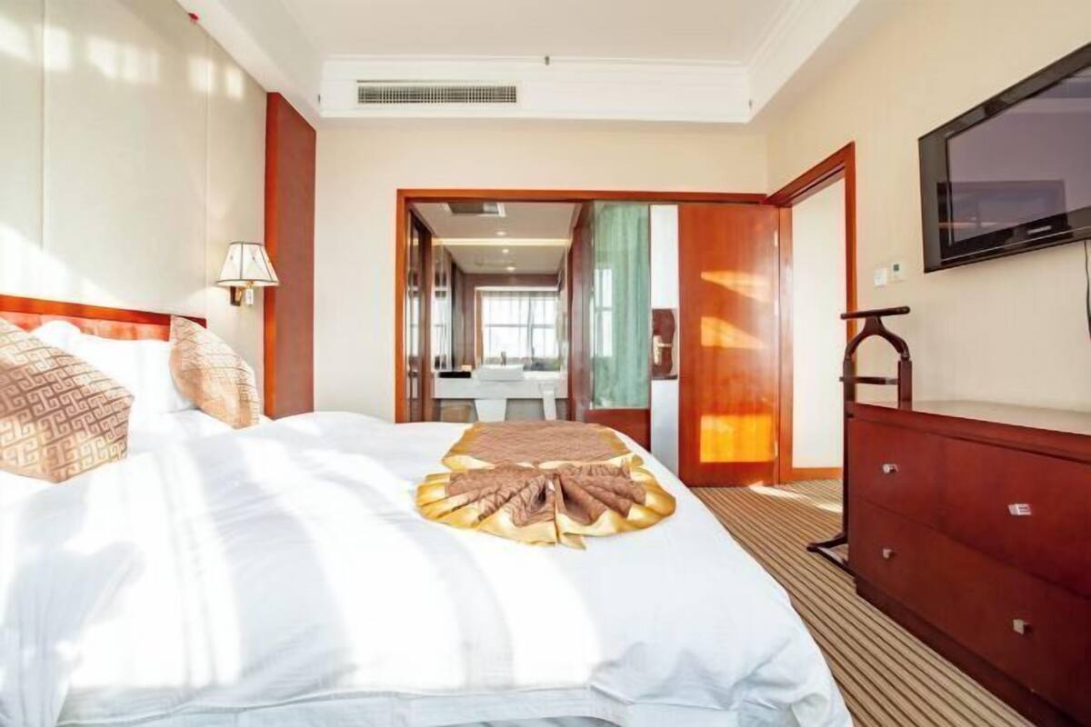 A hotel room with a large bed, a TV mounted on the wall, and a wooden dresser.