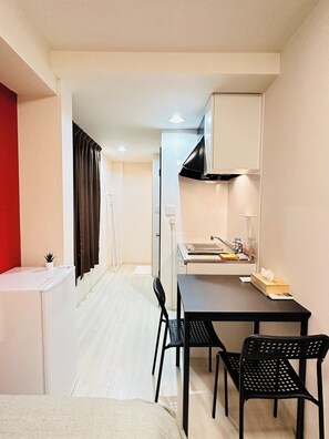 A compact room with a bed, a small table with chairs, a kitchenette, and a red accent wall. - Twin Room / Osaka Ōsaka (Osaka)