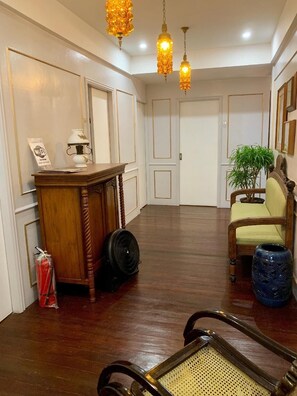 Una habitación amplia con piso de madera, un escritorio de madera, un ventilador, una silla y una planta en maceta.