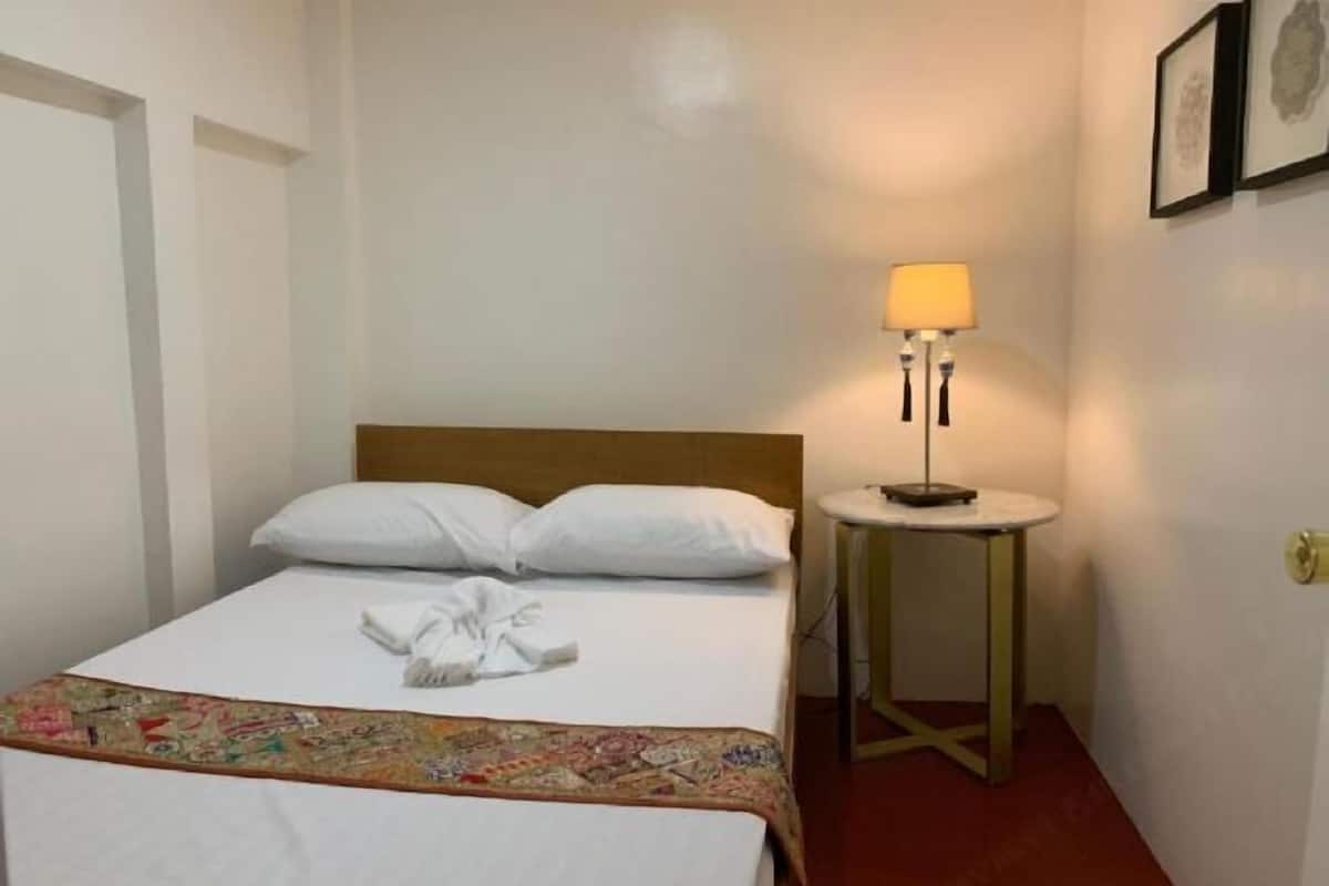 A hotel room with a bed, a bedside table with a lamp, and a wall-mounted picture.