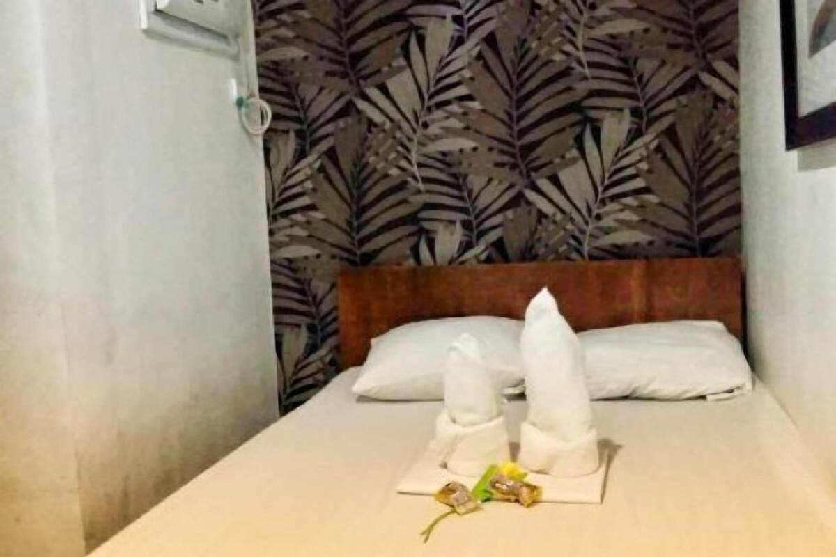A hotel room with a bed, pillows, a wooden headboard, and a wall with a leaf pattern.