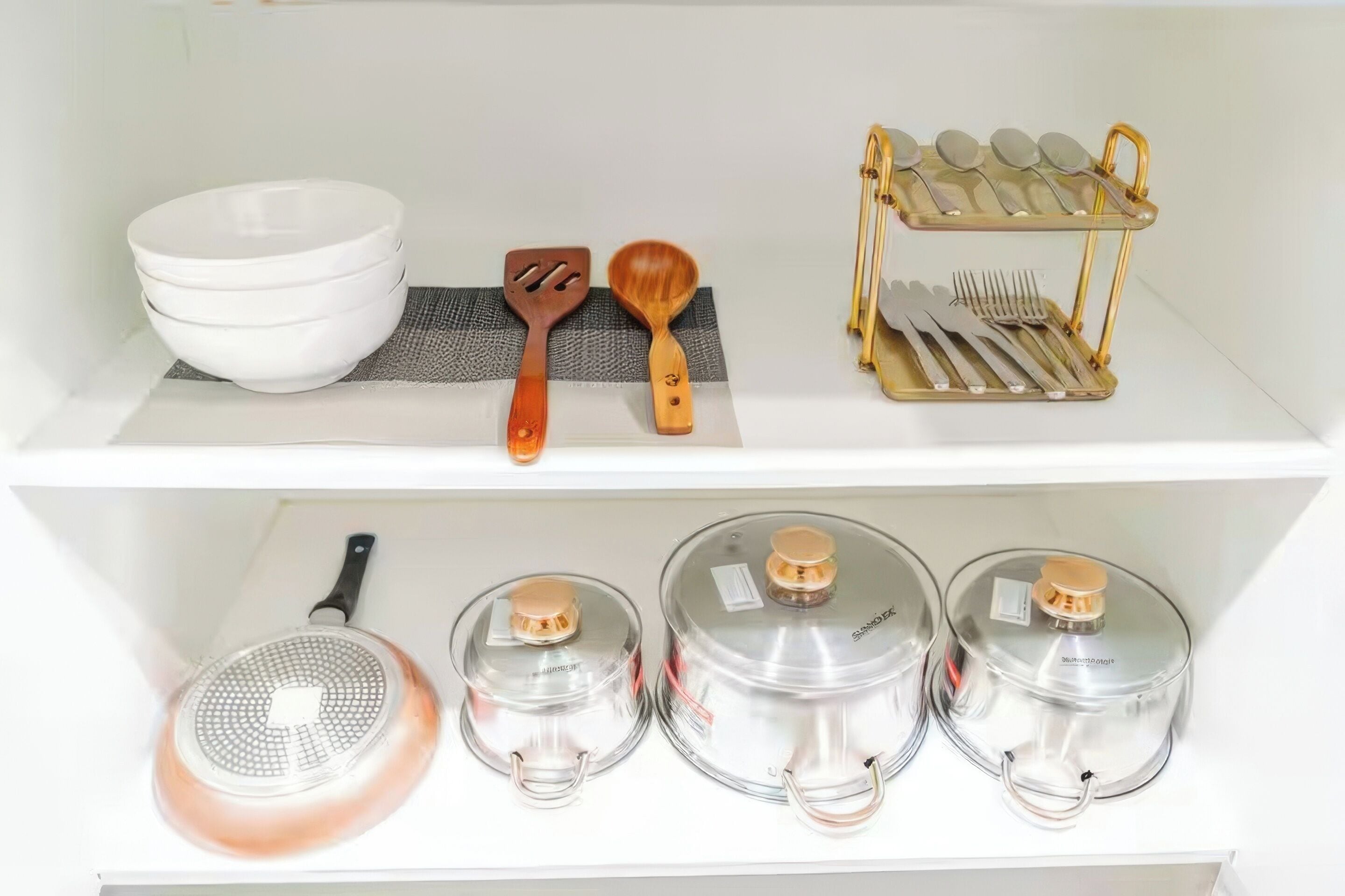A kitchen shelf with white bowls, a wooden spatula, a wooden spoon, a metal utensil holder, and three stainless steel pots.