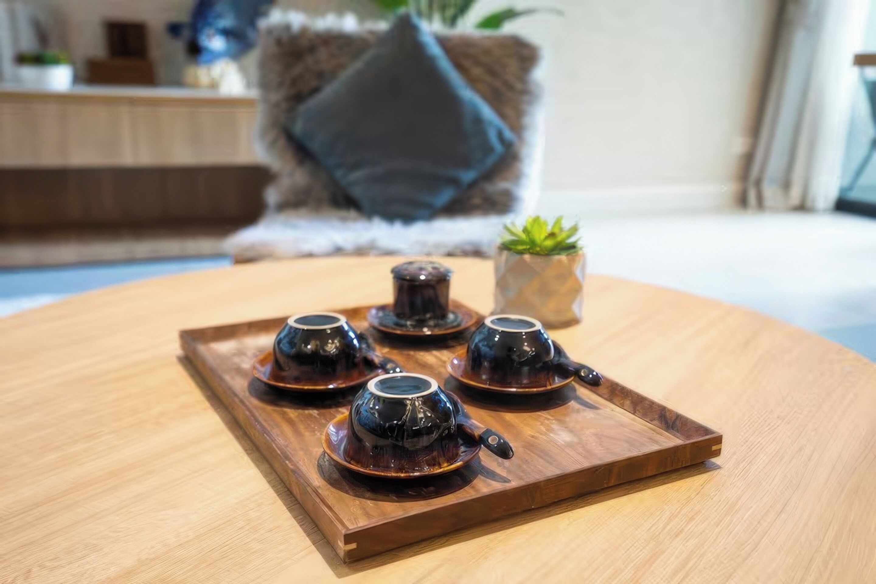 A tray with four dark ceramic cups and saucers on a wooden table.