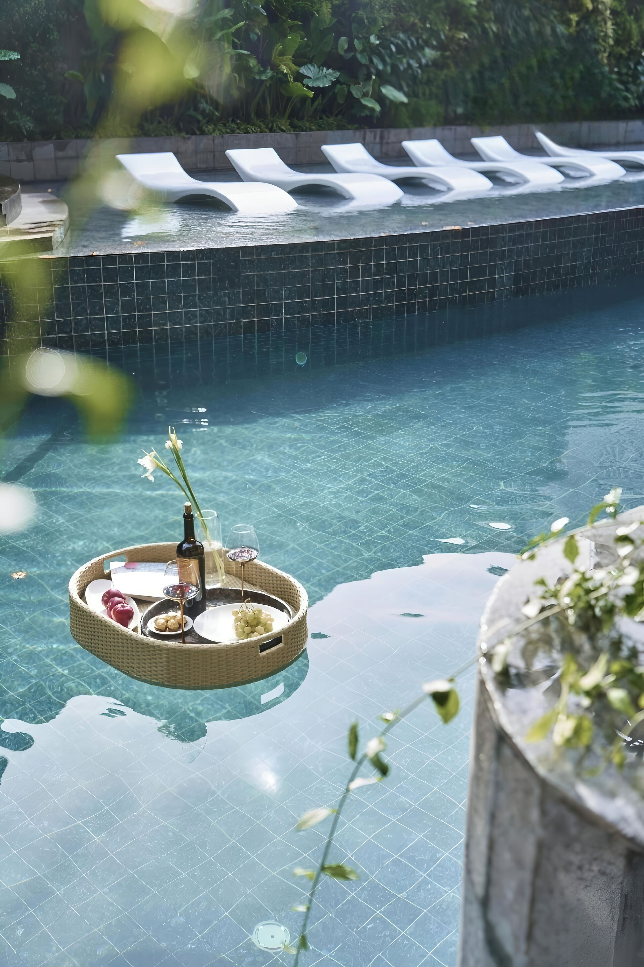 A pool with lounge chairs and a floating tray with a bottle and glasses.
