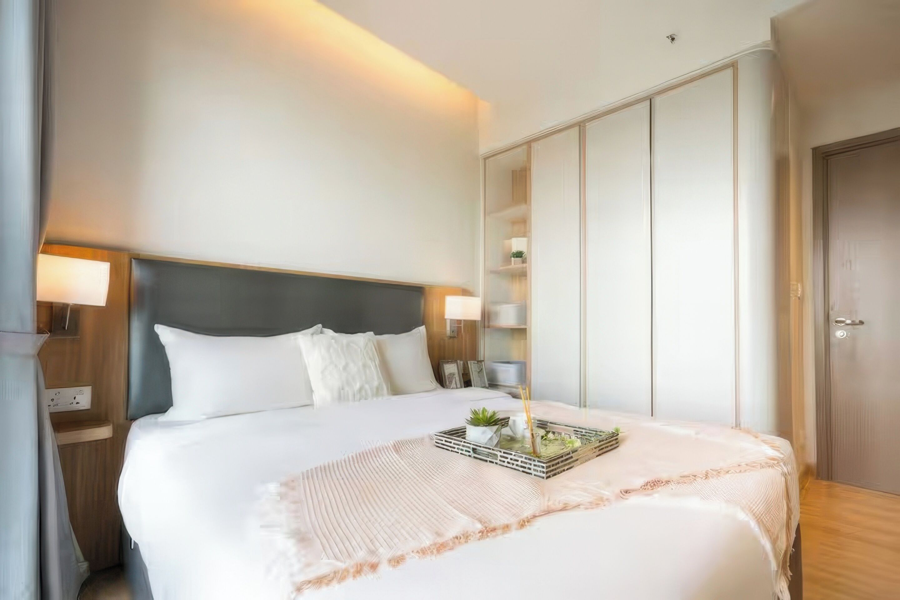 A hotel room with a large bed, bedside lamps, a wardrobe, and a bedside table.