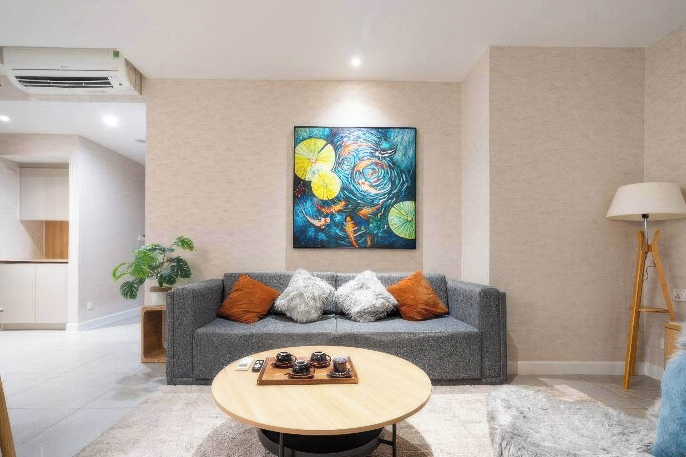 Een moderne woonkamer met een grijze bank, een ronde salontafel en een kleurrijk abstract schilderij aan de muur.