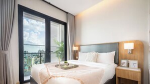 A hotel room with a large bed, a nightstand, a window with curtains, and a view of the city. - Imperial Elegance Zenity D1 (Ho Chi Minh City)