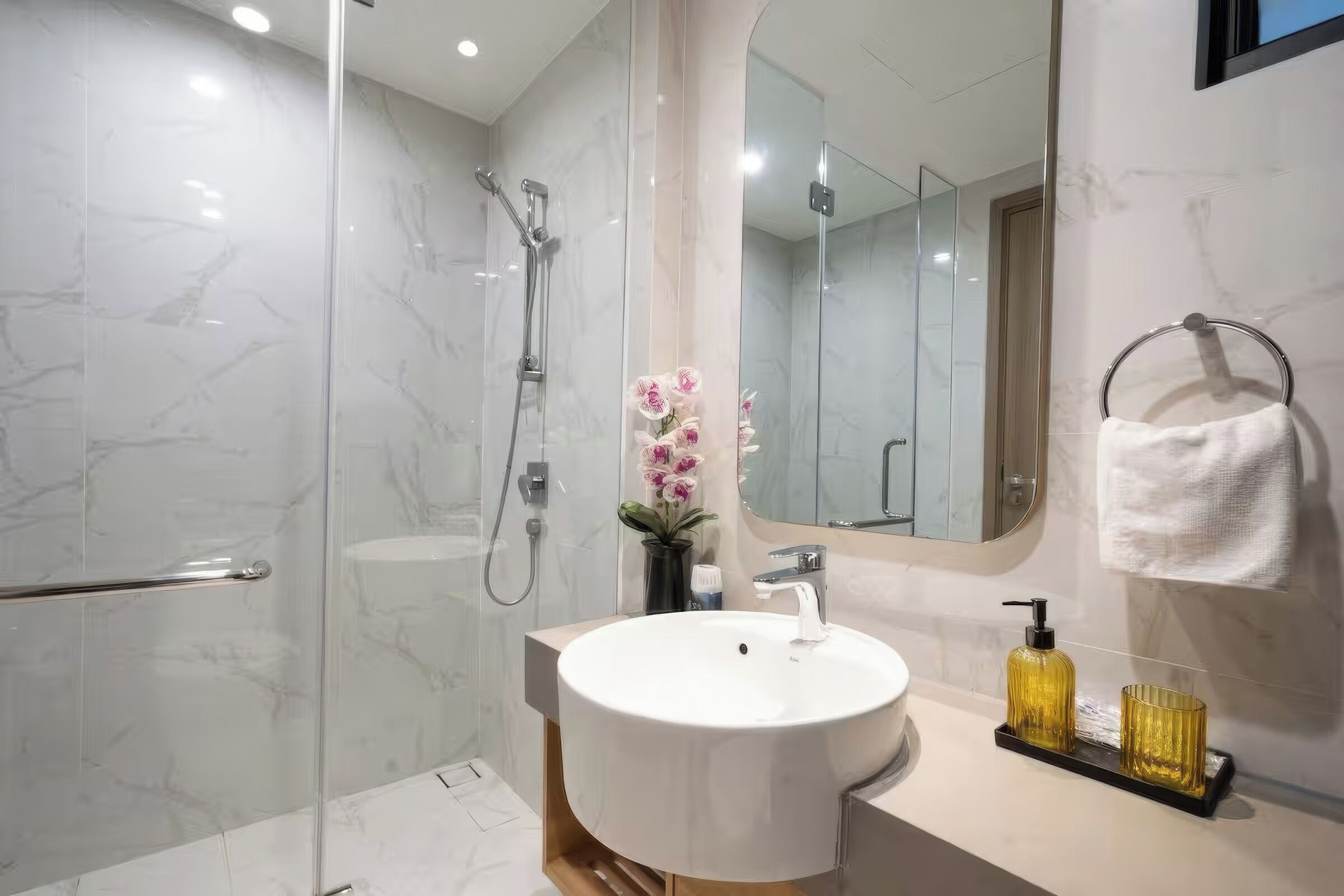 A modern bathroom with a glass-enclosed shower, a white sink, and a mirror above it.