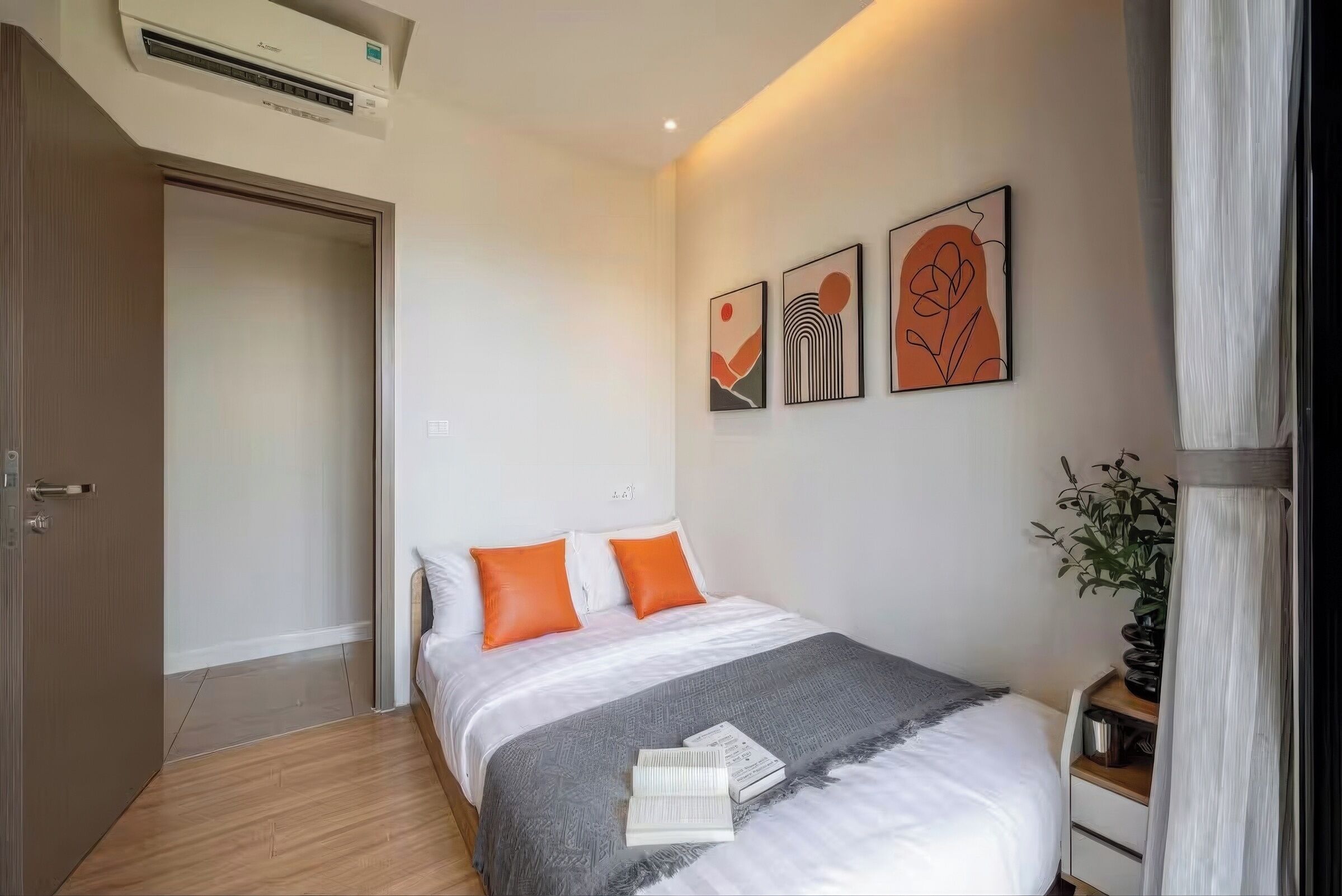 Een slaapkamer met een bed, nachtkastje, potplant en een wandairconditioner.